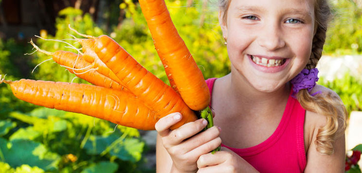 smiling girl holding fresh carrots