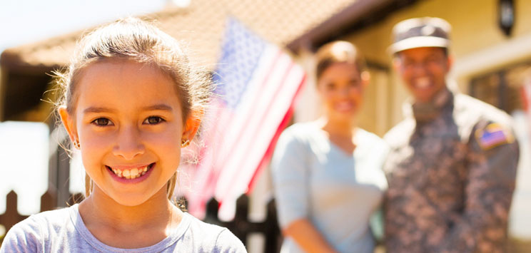 girl with military family standing in front of house with American flag